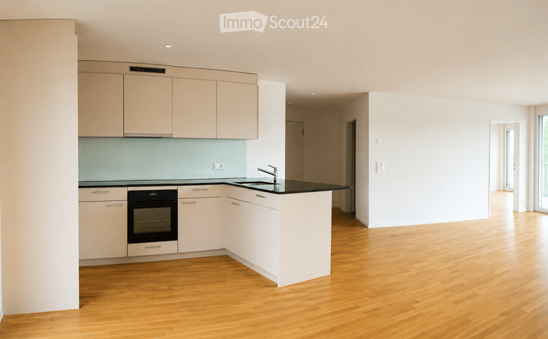 Modern kitchen with light-colored cabinets, a black countertop, and a built-in oven. The floor is made of light wood, and the space is bright and open.