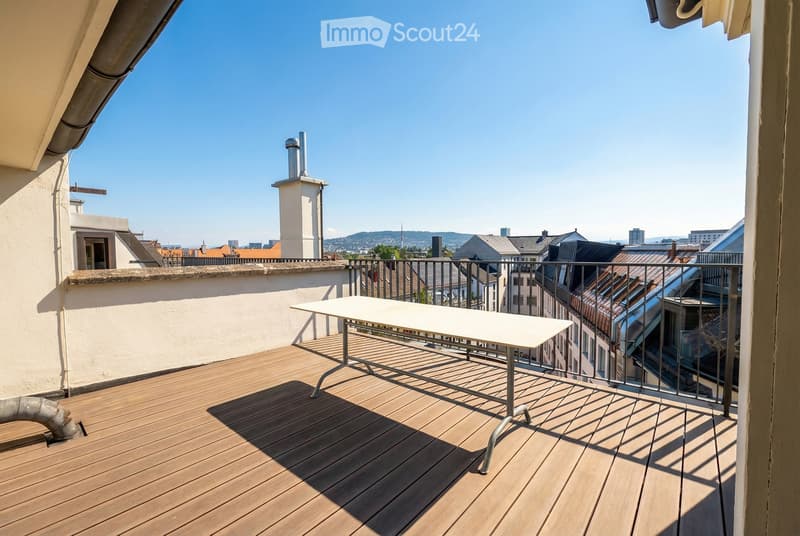Wooden deck with a white table, metal railing, and cityscape view.