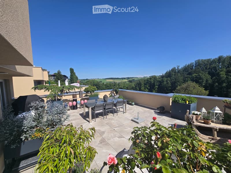 Balcony with a dining table, chairs, lanterns, and potted plants, overlooking a scenic landscape.