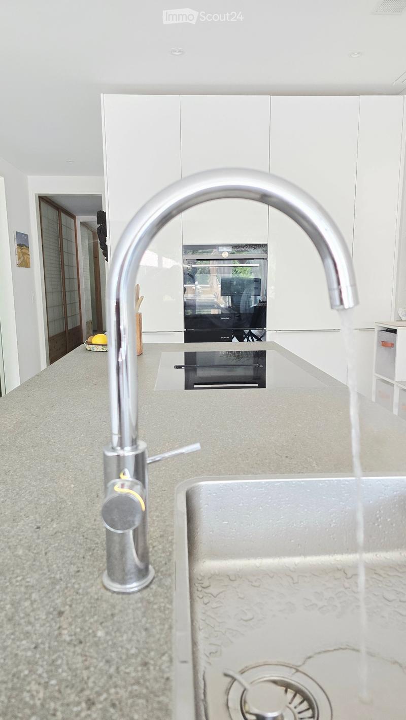 Modern kitchen with white cabinets, stainless steel faucet, and built-in oven. Countertop has a sink and a small cutting board with a lemon and wooden utensils.