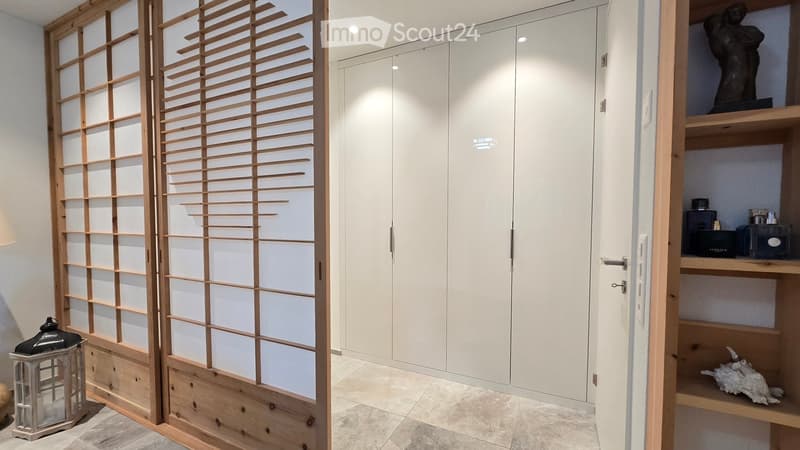 Modern hallway with white built-in wardrobes, a wooden sliding door with a grid pattern, and a decorative lantern on the floor.