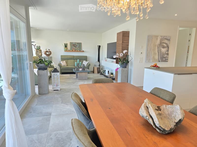 Open-plan living and dining area with a green sofa, wooden coffee table, dining table with chairs, and decorative items including a chandelier and artwork.