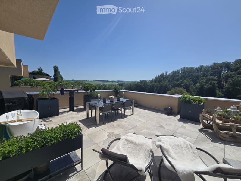 Spacious outdoor terrace with tiled flooring, a dining set, lounge chairs, a bathtub, and potted plants, offering scenic views of greenery and countryside.