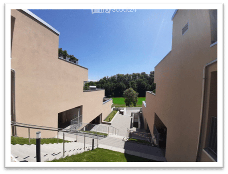Courtyard view of a modern building complex with a staircase leading up, surrounded by greenery and a clear blue sky.