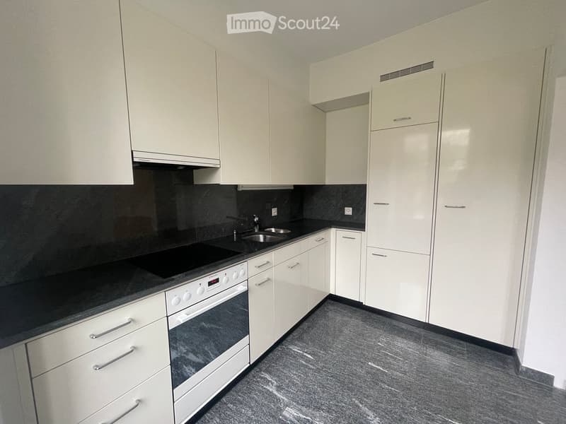 Modern kitchen with white cabinets, black countertops, and stainless steel appliances including an oven and sink.
