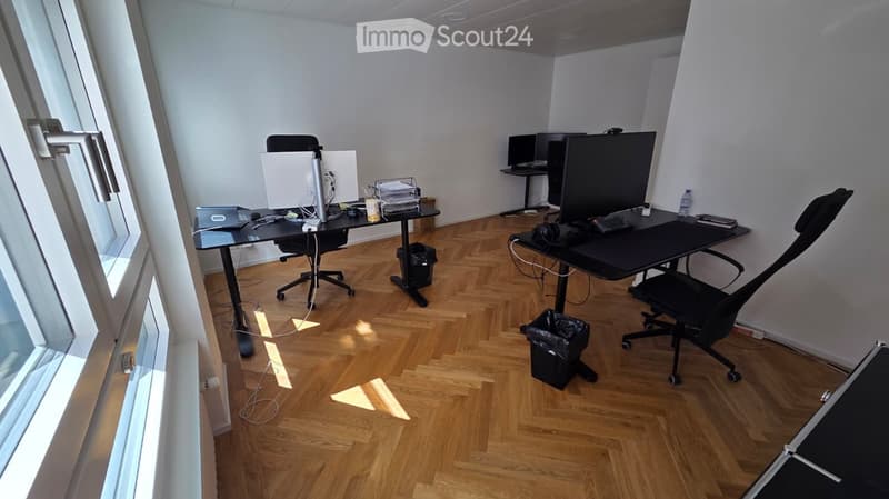 Office space with wooden flooring, two desks, chairs, laptops, monitors, and office supplies.
