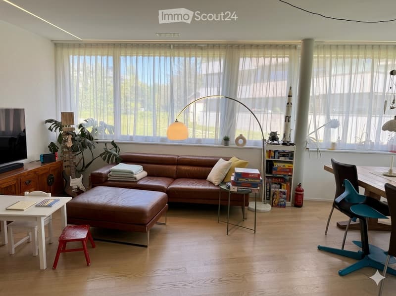Bright living room with large windows, leather sofa, ottoman, coffee table, floor lamp, guitar, and various decorative items.