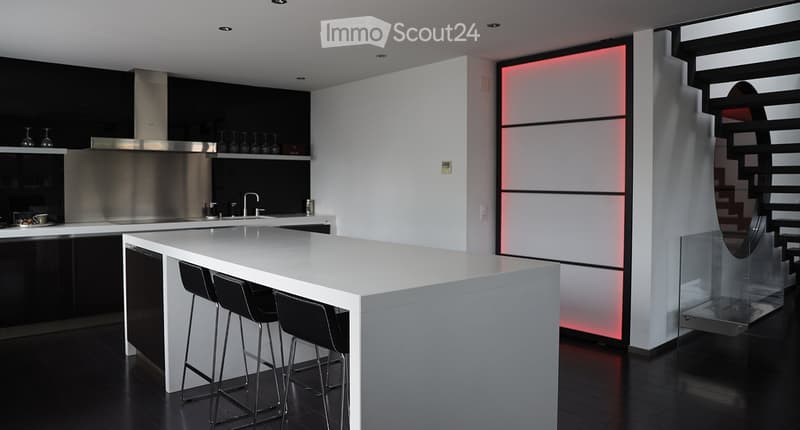 Modern kitchen with white island, black stools, stainless steel range hood, sink, and wine glasses on shelves.
