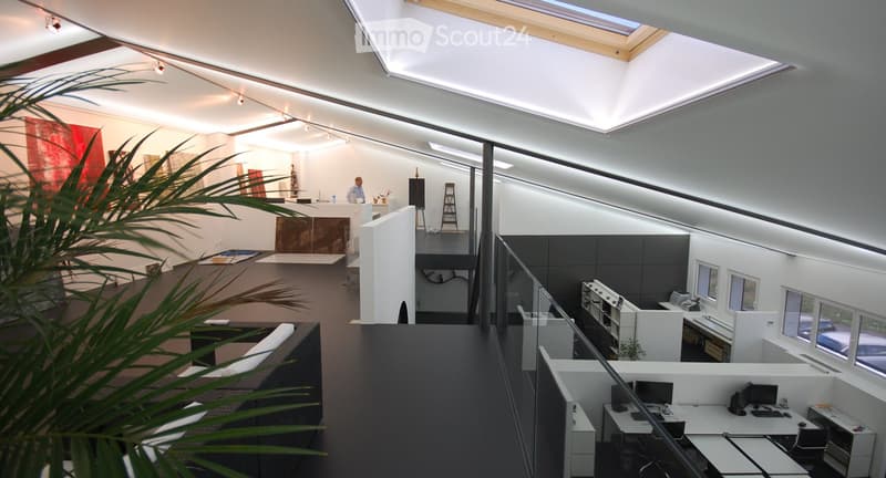 Modern office space with desks, chairs, sofas, and a reception area. Features large windows, a skylight, and contemporary decor.