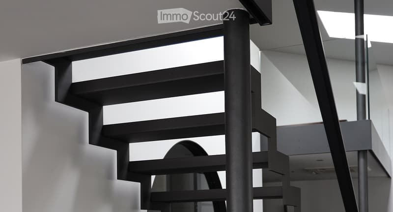 Modern black staircase with sleek design and glass railings, leading upwards in a bright, contemporary interior.