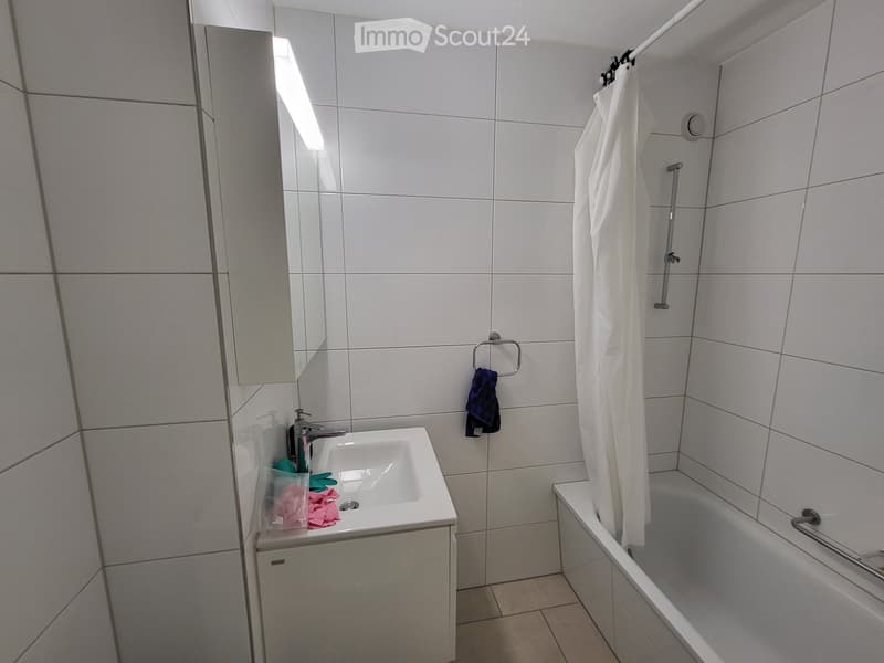 Modern bathroom with white tiles, a sink with a mirror, a bathtub with a shower curtain, and a towel hanging on a ring.
