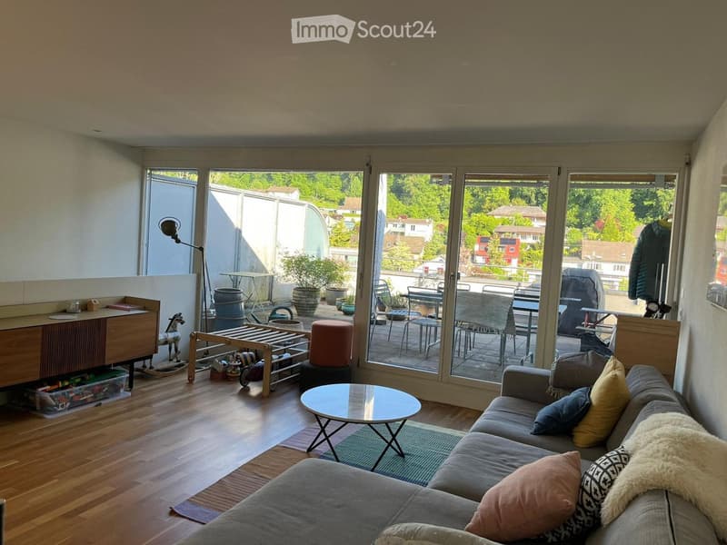 Bright living room with large sliding glass doors leading to a balcony, featuring a grey sofa, coffee table, small round table, and various decorative items.