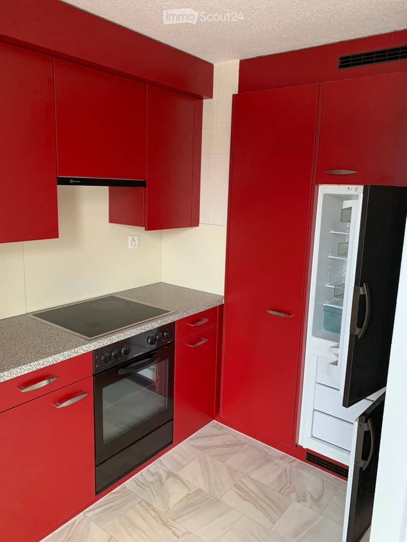 Red kitchen cabinets, white countertop, induction hob, black oven, open refrigerator, modern appliances