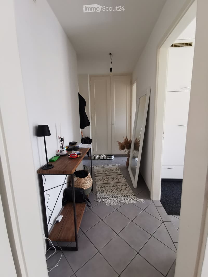 A modern hallway with a wooden table, black lamp, mirror, patterned rug, and coat hanging on the wall.