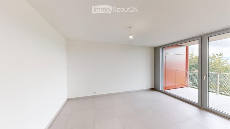 Empty room with white walls, tiled floor, and large sliding glass doors leading to a balcony with a view of trees and the ocean.