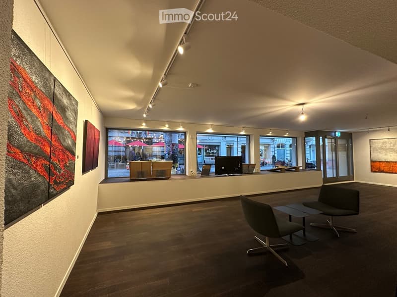 Modern, minimalist room with wooden flooring, large windows, and contemporary furniture including chairs, a stool, and a screen.