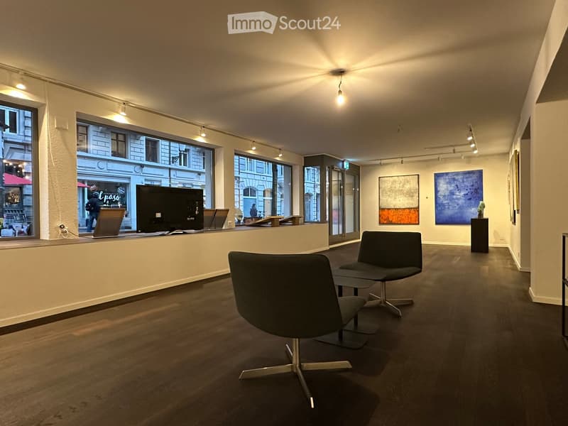 Modern, minimalist room with dark wooden flooring, large windows, and contemporary furniture including chairs, a stool, a screen, a table, and artwork.