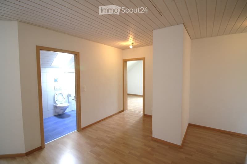 Empty hallway with wooden flooring, white walls, and two open doors leading to a bathroom and another room.