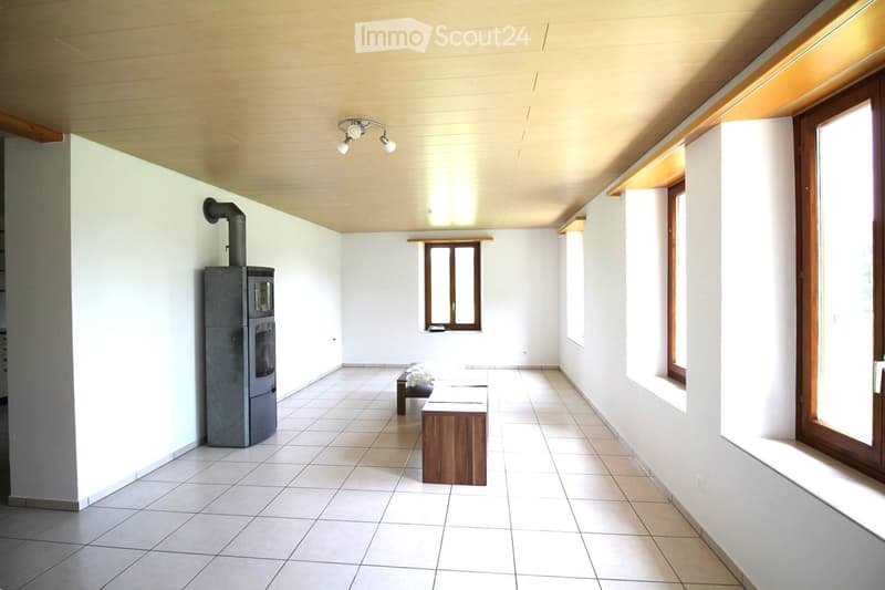 The image shows an unfurnished room with white walls, tiled flooring, and a fireplace. There are two wooden benches placed in the center of the room, and a ceiling light fixture is visible.