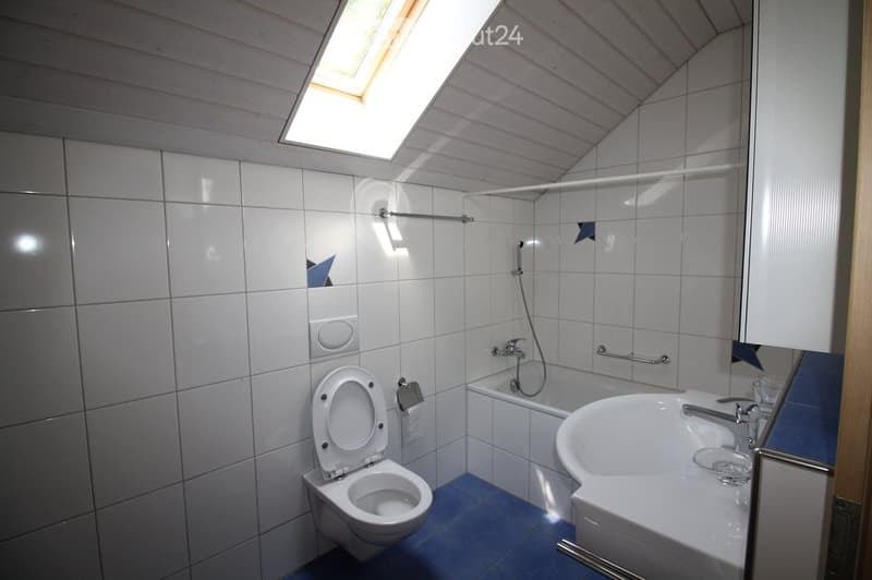 Modern bathroom with white tiles, a toilet, a sink, a bathtub, and a skylight window providing natural light.