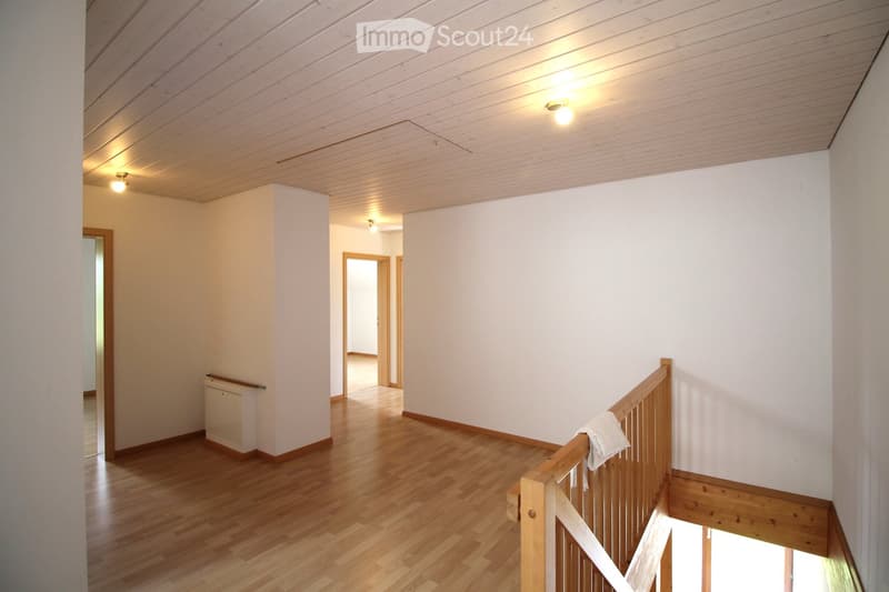 Empty hallway with wooden flooring, white walls, and a staircase leading upwards. The ceiling is paneled with recessed lighting.