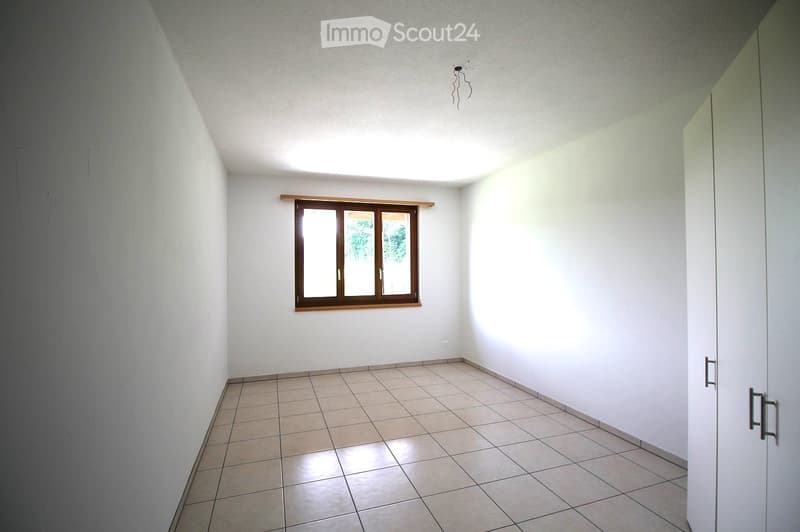 Empty room with white walls, tiled floor, and a single window with wooden frame. No furniture or equipment present.