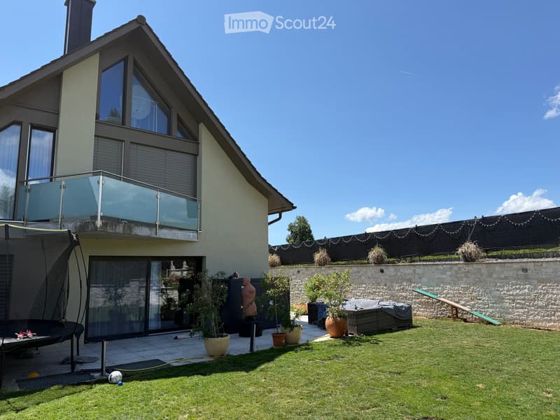 A well-maintained garden with a grassy lawn, potted plants, a trampoline, and a covered seating area near the house.