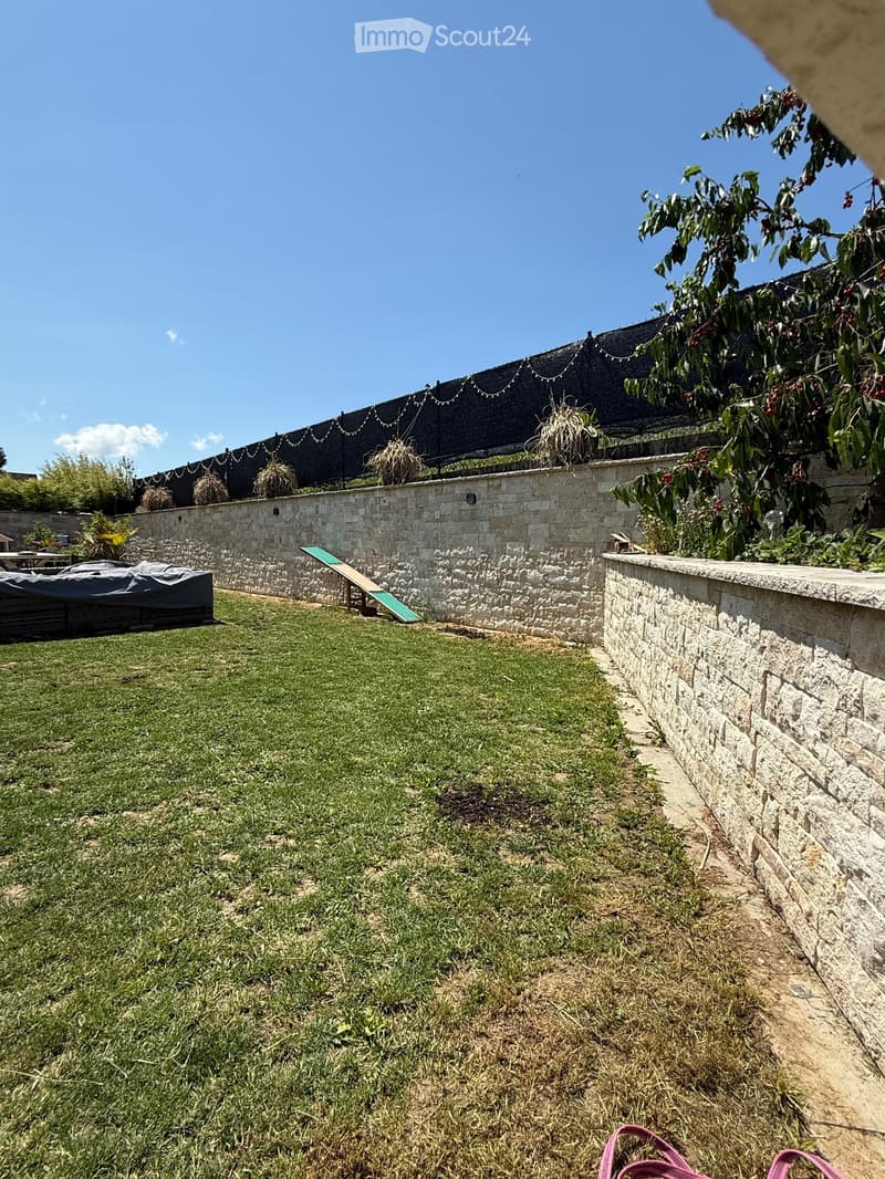 Well-maintained garden with a grassy lawn, stone walls, a small slide, and a covered seating area with string lights.