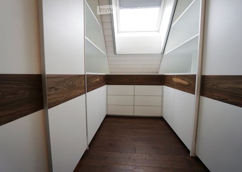 Modern hallway with white and wood paneling, wooden floor, and a skylight at the top.