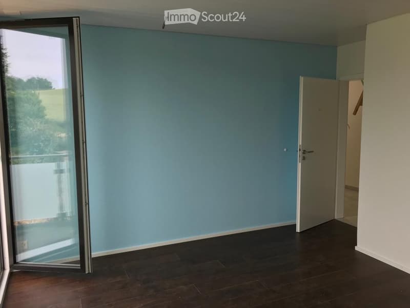 Empty room with light blue walls, dark wooden flooring, and a large sliding glass door leading to a balcony.