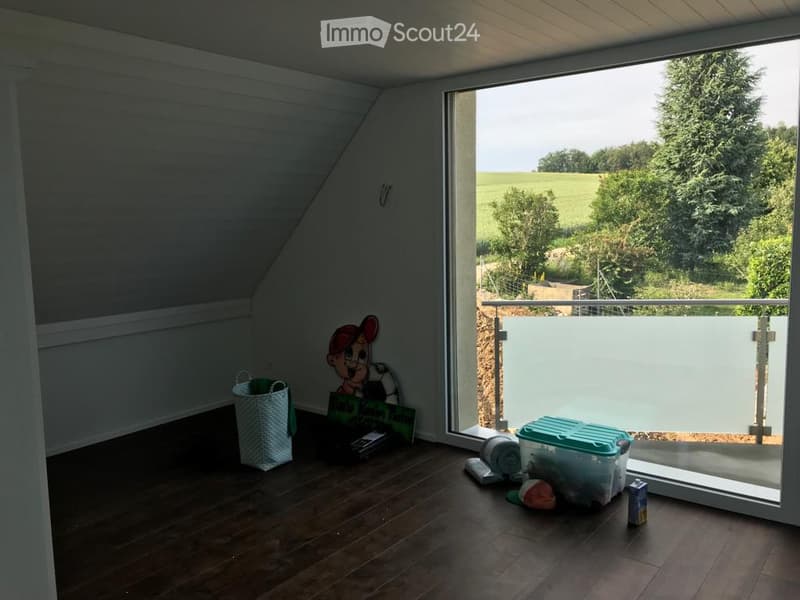 Bright, wooden-floored room with large windows offering a scenic view of greenery. Contains a basket, storage bin, toy, books, and a cup.