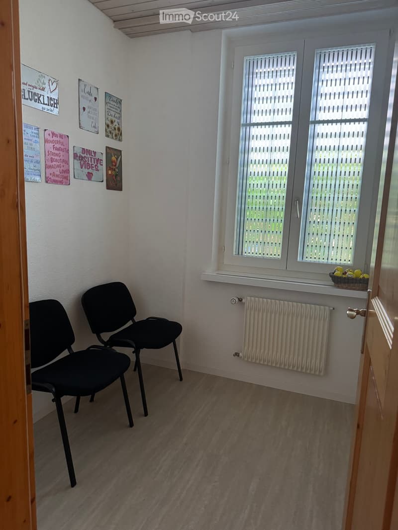 Small, unfurnished room with two black chairs, a radiator, a window with blinds, and motivational posters on the wall.