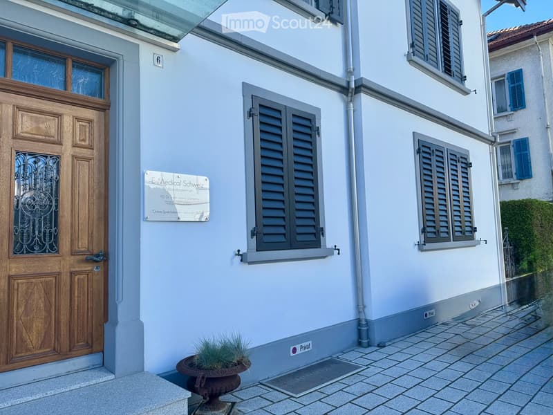 Light blue building with wooden door, grey shutters, and a sign reading "E-Medical Schweiz" and "Privat".