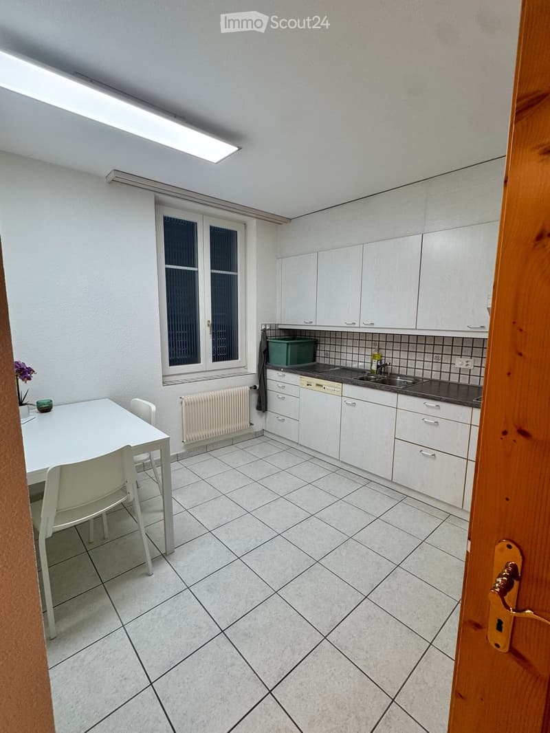 Modern kitchen with white cabinets, tiled floor, sink, dishwasher, and a small dining area with a table and chairs.