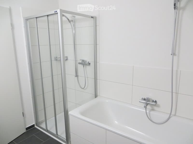 Modern bathroom with a white bathtub, glass shower stall, and chrome fixtures.