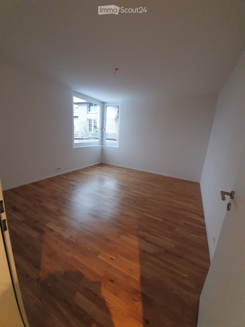 Empty room with wooden flooring and white walls, featuring a window with white frame and a door with silver handle.