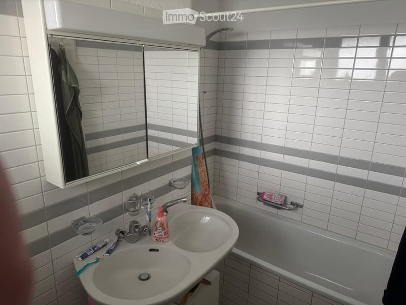 Bathroom. Bathroom with white tiled walls, a double sink, a bathtub, a mirror, and various toiletries including toothbrushes, toothpaste, and a towel.