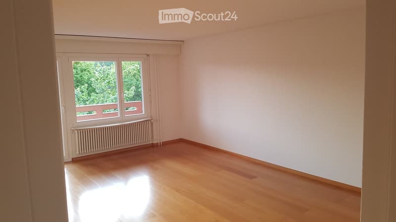 Empty room with wooden flooring, white walls, and a window with a view of greenery. No furniture or equipment is present.