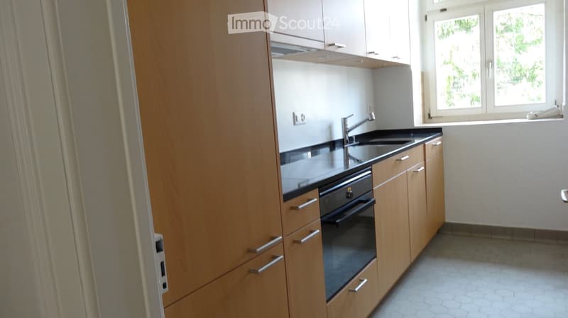 Modern kitchen with light wooden cabinets, black countertop, stainless steel sink and faucet, and built-in oven.