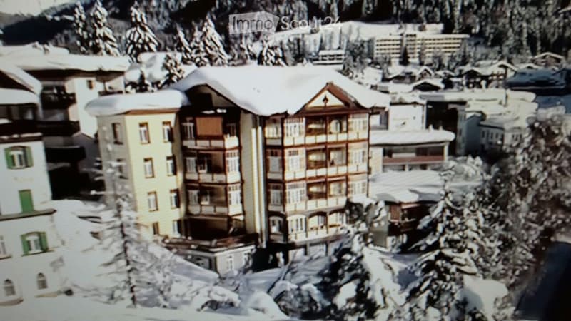 A multi-story building with balconies and snow-covered surroundings, likely a residential or hotel structure in a mountainous area.