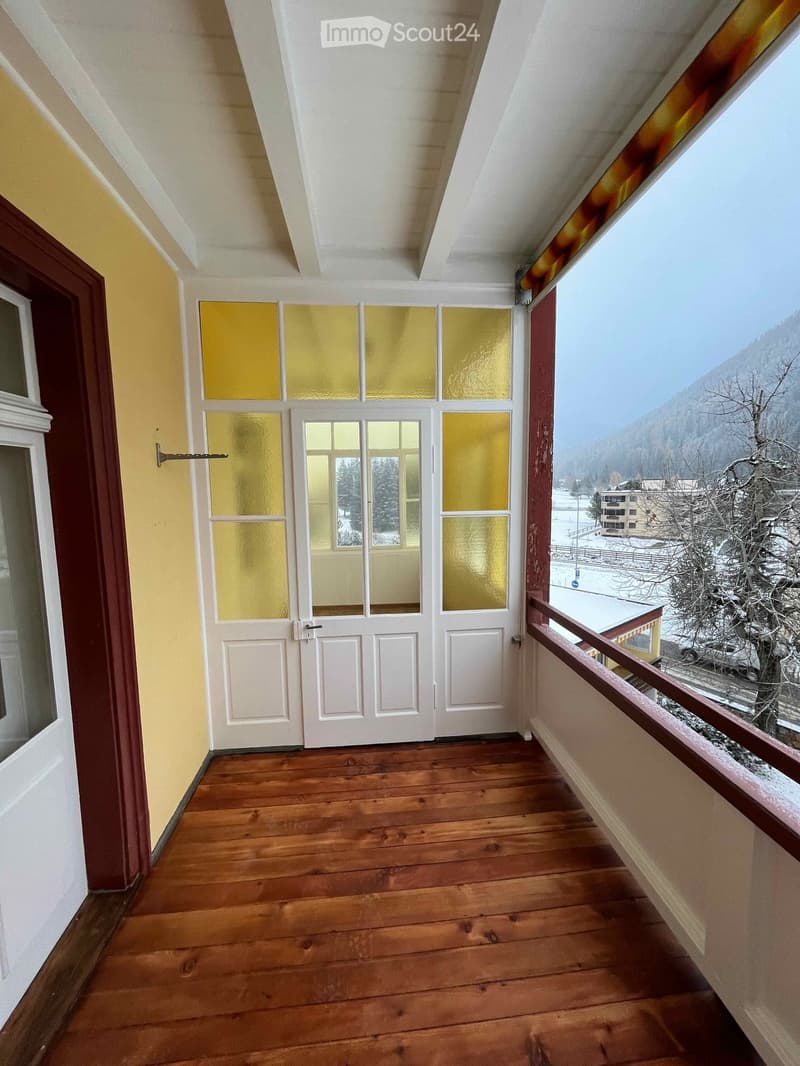 Balcony with wooden flooring, white double doors with frosted glass panels, and a wooden railing overlooking a snowy landscape.