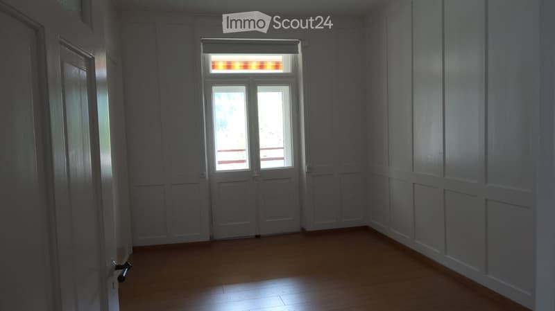 Empty hallway with wooden flooring, white paneled walls, and a double door leading to a balcony area.