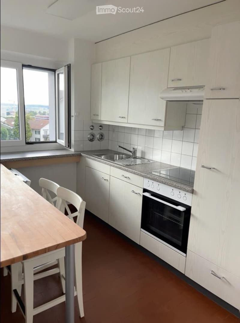 Modern kitchen with white cabinets, granite countertops, stainless steel sink, and built-in oven. Includes a small dining area with a wooden table and white chairs.
