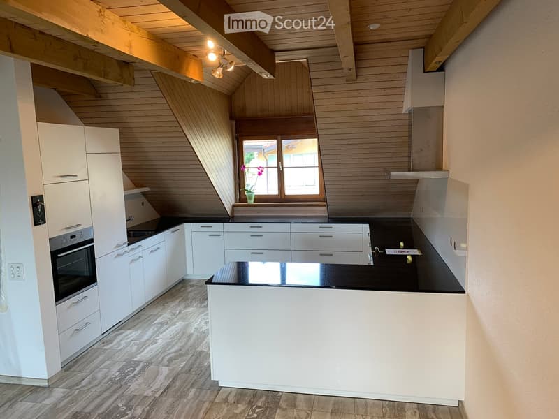 Modern kitchen with white cabinets, black countertop, and a window with a flower pot on the sill. The ceiling has exposed wooden beams and warm lighting.