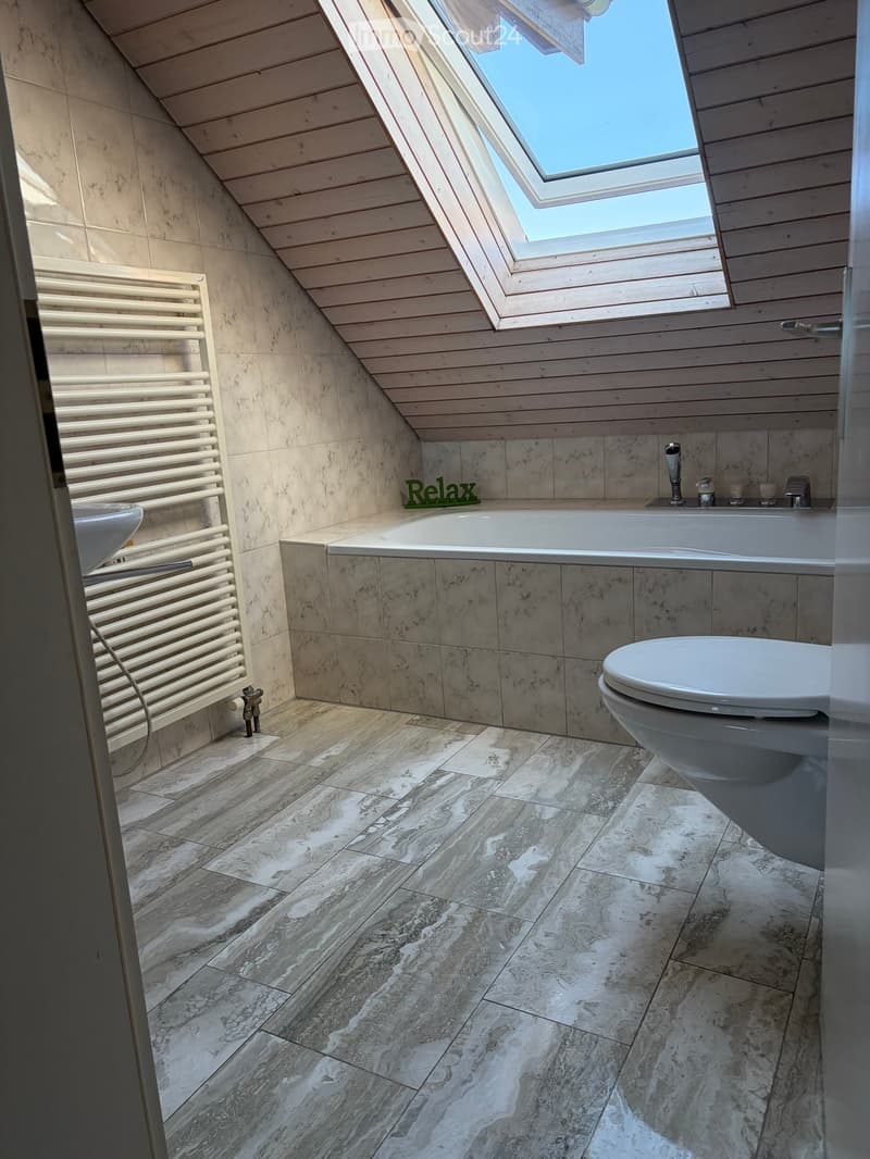 Modern bathroom with marble tiles, a bathtub, toilet, sink, and a radiator. Features a skylight window and a sleek design.