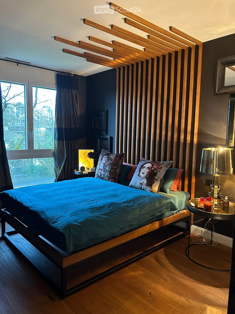 Bedroom with wooden bed, blue bedding, wooden headboard, nightstands with lamps, decorative pillows, and a window with curtains.
