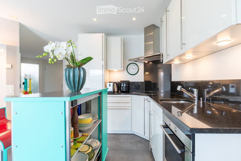 Modern kitchen with white cabinets, stainless steel appliances, a central island with a turquoise countertop, and a vase with white flowers on the island.