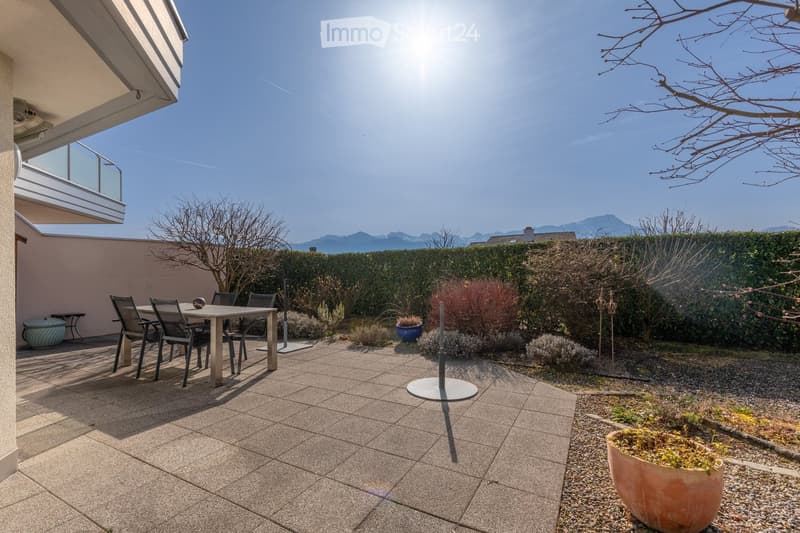 Well-maintained patio with a dining table and chairs, surrounded by neatly trimmed hedges, potted plants, and a gravel area.