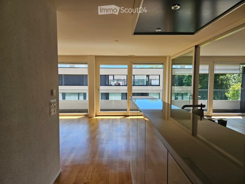 Empty room with wooden flooring, large windows, and a view of a swimming pool and greenery outside.
