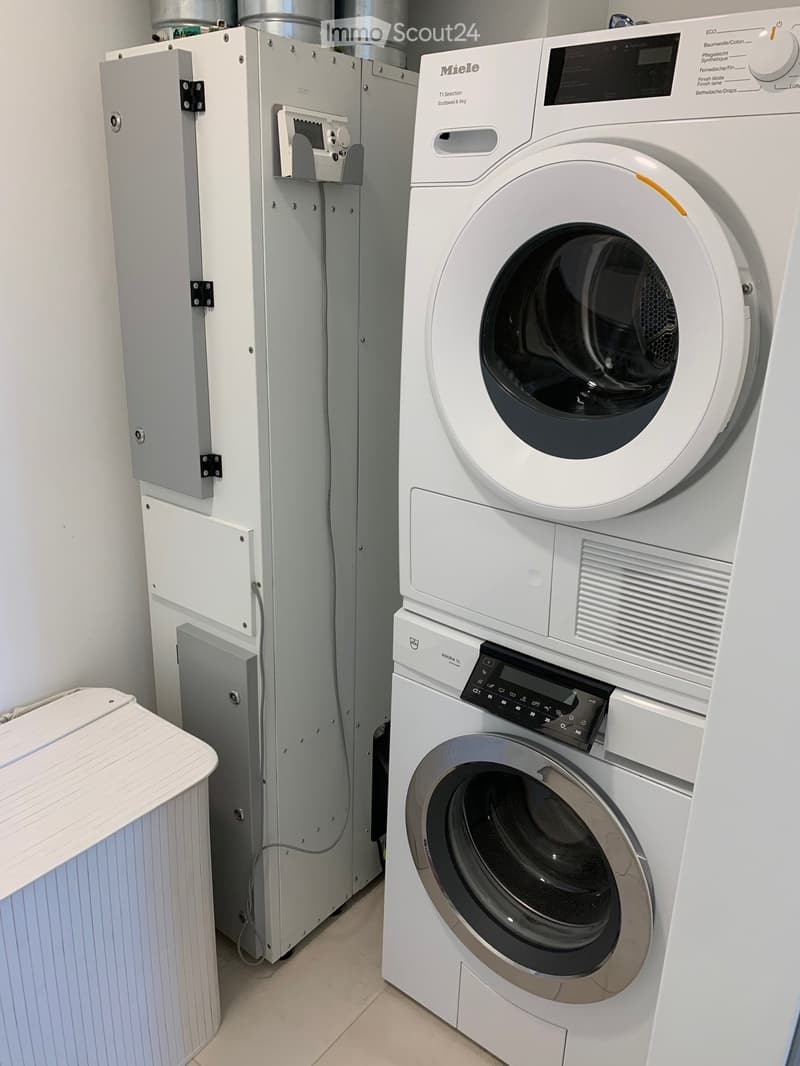 Modern bathroom with a white washing machine and dryer stacked vertically, featuring a control panel and a sleek design.